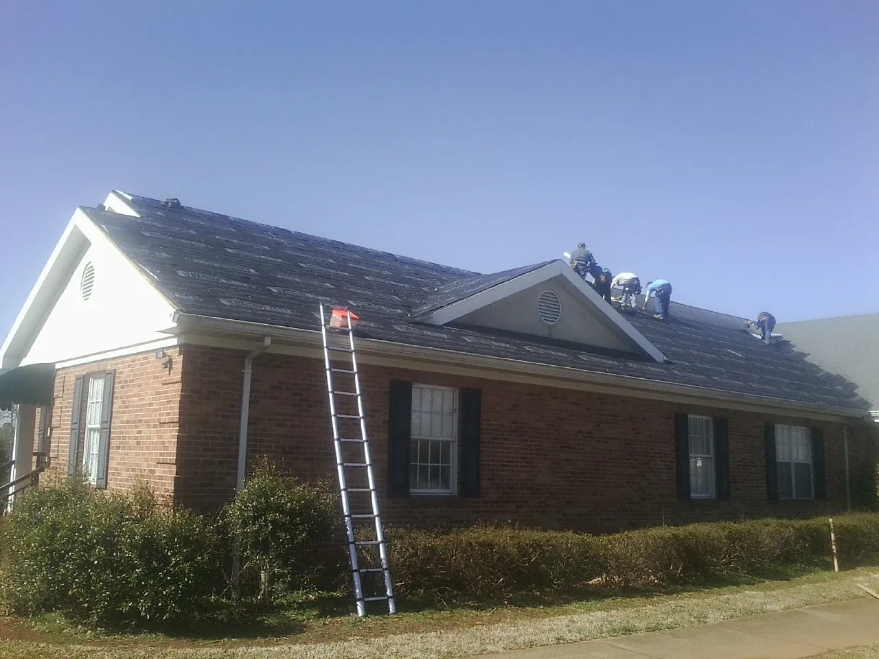 Crew tearing shingles off a brick ranch roof with a ladder set — Metal Roof Repair work by our crew in Fairchild Air Force Base