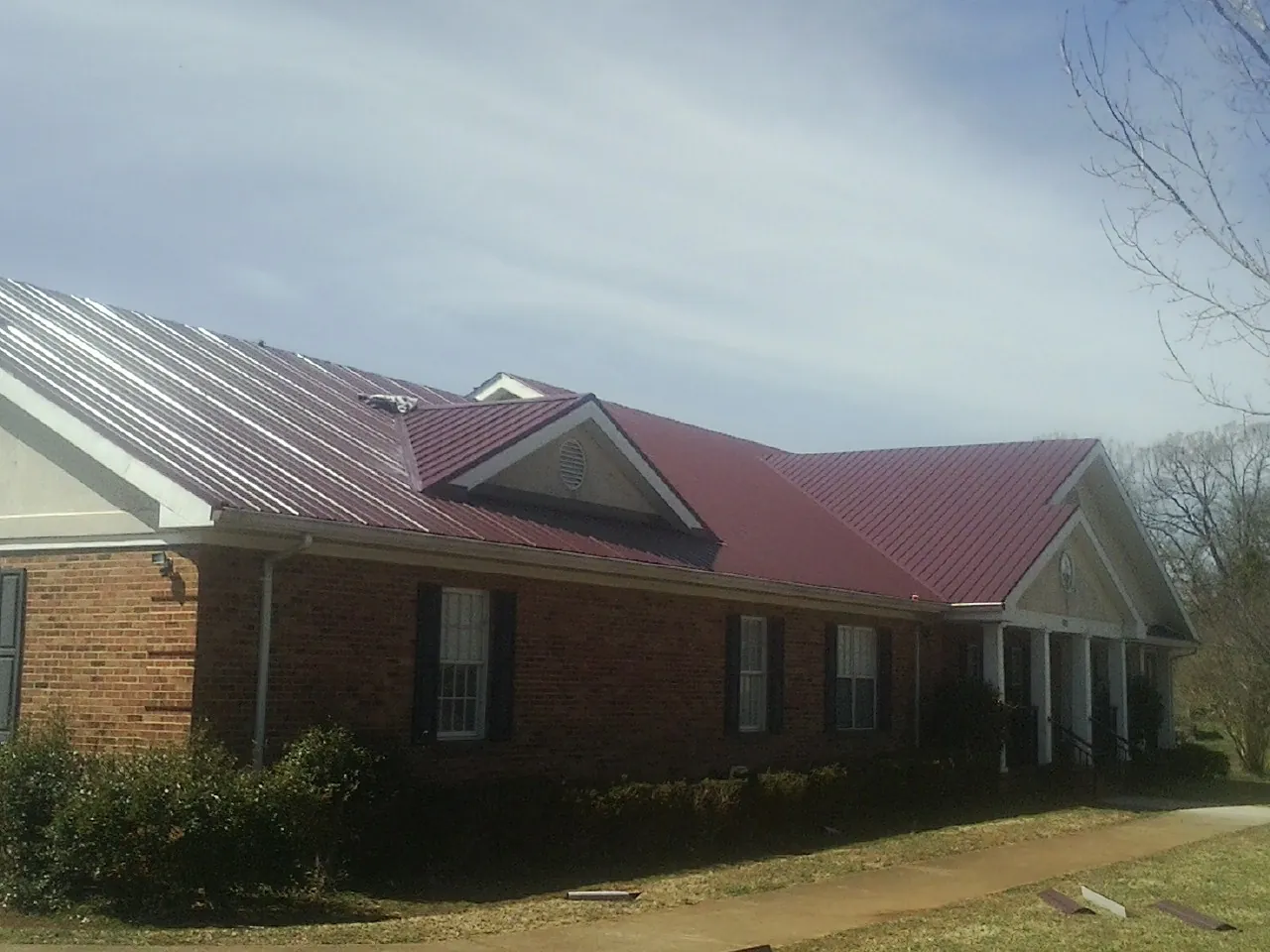 Red metal roof with gabled entries on a long brick building, from a Hail Damage Roof Repair job in Fairchild Air Force Base