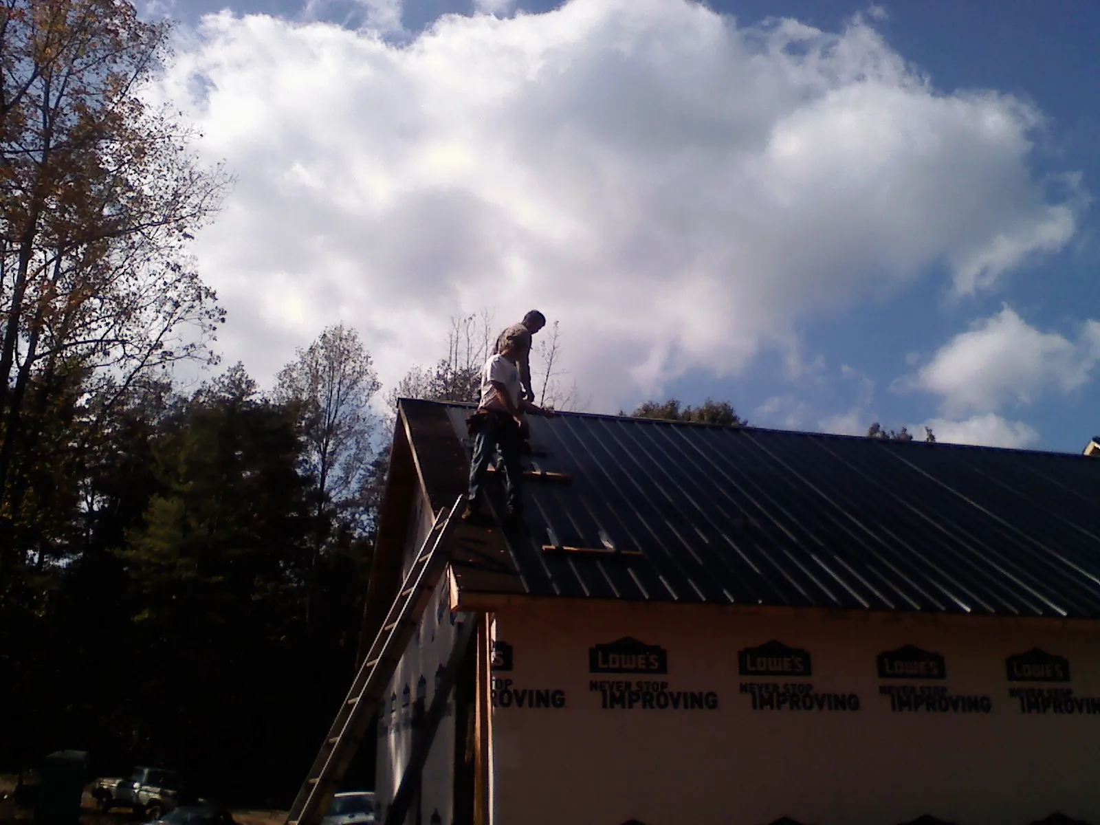 Roofer fastening dark metal panels high against a cloudy sky, from a Roof Inspection job in Fairchild Air Force Base