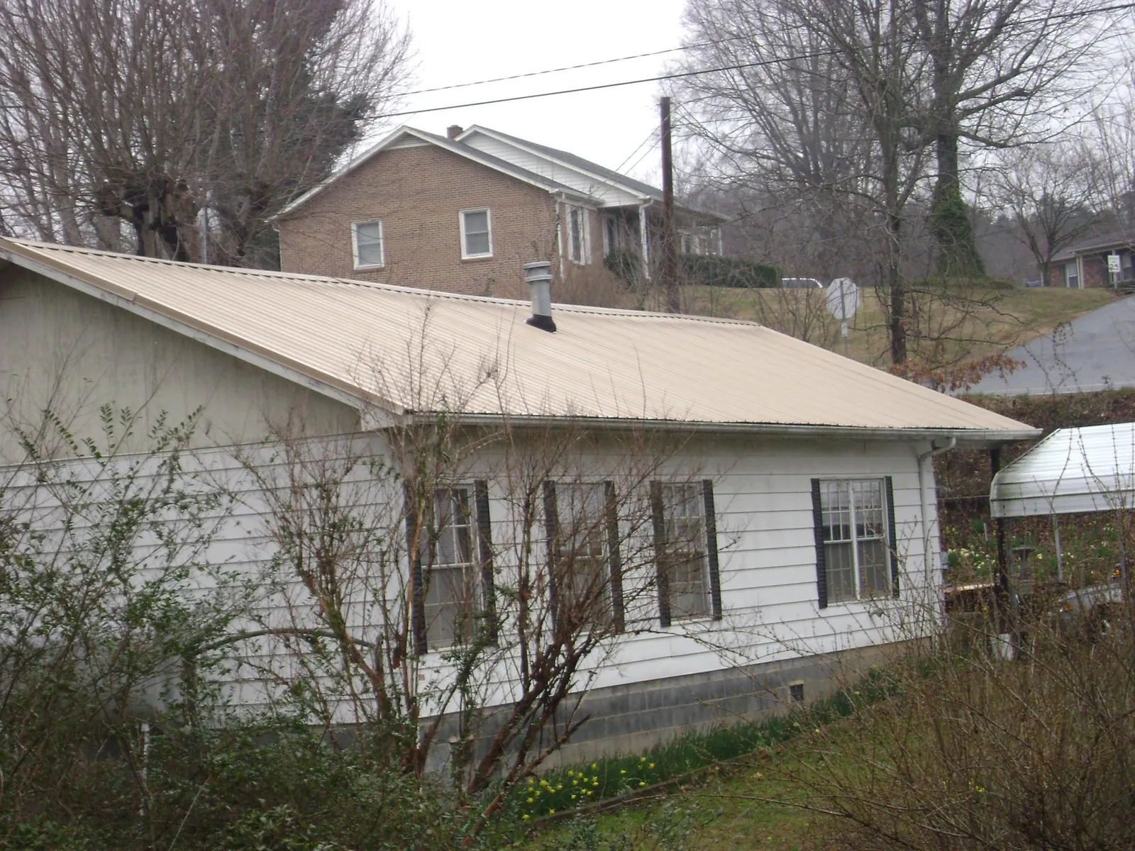 Tan metal roof on a white sided house set into a hillside — Commercial Roofing by Roofing Brothers in Fairchild Air Force Base